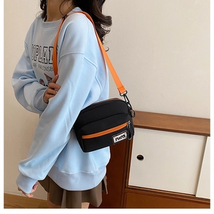 Detail of black canvas crossbody bag featuring contrasting orange strap and front pocket