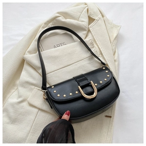 Détail du sac à bandoulière noir avec rivets dorés et boucle en U sur un blazer blanc