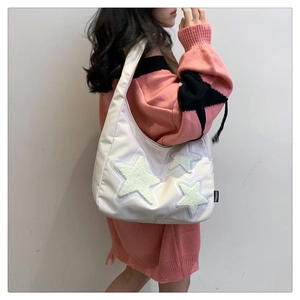 Close-up of white canvas tote bag with yellow plush stars and fashion label detail
