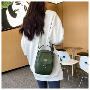 Rear view of a model wearing a dark green nylon crossbody bag with multiple zip pockets