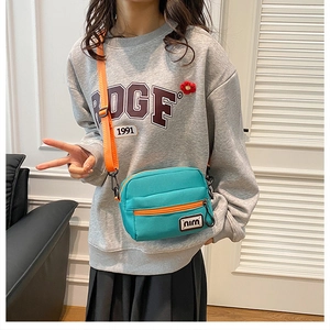 Detail of mint green canvas crossbody bag with orange contrast straps and adjustable buckle