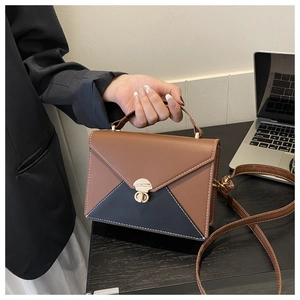Détail d'un sac enveloppe bicolore avec surpiqûres blanches et fermoir rotatif en métal