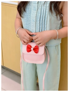 Mini sac bandoulière rose pour fille avec nœud rouge présenté par un enfant mannequin en studio
