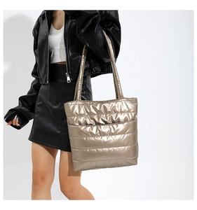 Detail of a metallic quilted tote bag in champagne gold shown on a model's shoulder