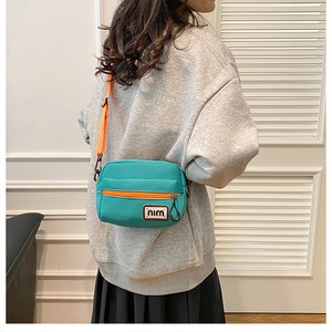 Detail of green canvas crossbody bag with orange zipper worn by a model in casual outfit