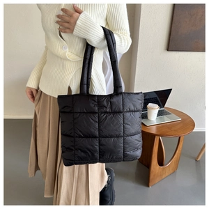 Lifestyle shot showing a black quilted tote bag on a wooden table near a laptop