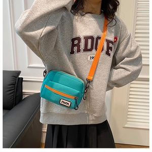 Close-up of mint green nylon crossbody bag with orange contrast zippers and strap