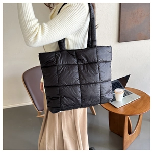 Close-up of black quilted puffer tote bag on a model in a cozy indoor lifestyle setting