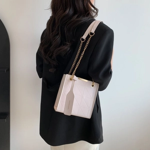 Detailed view of beige crossbody bag with quilted pattern and gold chain strap