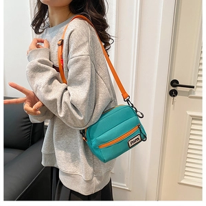 Detail of teal nylon crossbody bag with orange zipper and strap on a casual model