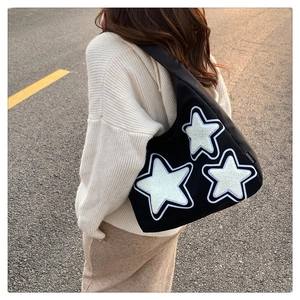 Detail of black canvas tote bag featuring white sequined star patches and fashion label