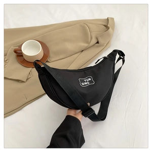 Minimalist black nylon crescent moon bag with logo detail on a neutral aesthetic background