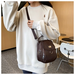 Detail shot of a dark brown Oxford cloth mini crossbody bag worn by a model in a cafe