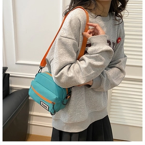 Detail of teal nylon crossbody bag with bright orange zippers and adjustable straps