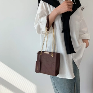 Detail of dark chocolate quilted crossbody bag with gold chain and shadow accents