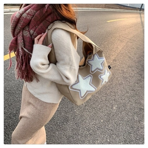 Close-up of beige canvas tote bag with white star patches worn by a model in soft sunset light