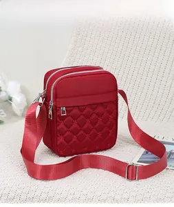 Red quilted nylon crossbody bag with three zipper compartments on a white textured chair