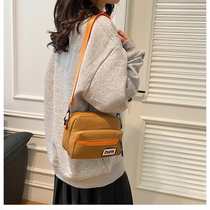 Detail view of a tan canvas crossbody bag with a bright orange strap and branding