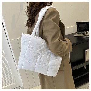 Detail view of a white quilted puffer tote bag shown on a model in a modern office