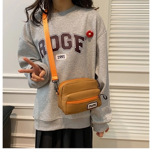 Detail of canvas crossbody bag with brown body and bright orange straps for daily casual style
