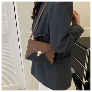 Détail d'un sac bandoulière bicolore avec fermoir rotatif doré et coutures contrastées