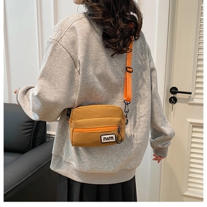 Detail of mustard yellow canvas crossbody bag with bright orange strap and letter patch