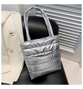 Detailed close-up of a silver metallic quilted puffer tote bag on a modern leather chair