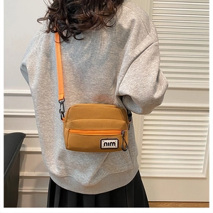 Detailed view of yellow canvas crossbody bag featuring adjustable orange strap and logo patch