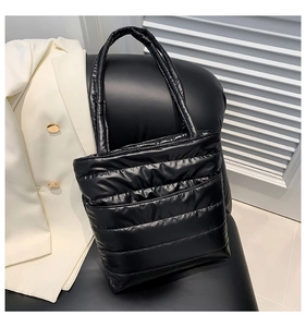 Detail of black quilted puffer tote bag with glossy finish on a dark leather chair