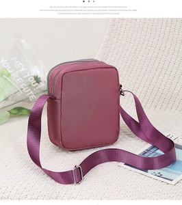 Detail view of burgundy nylon crossbody bag with dual zippers and wide woven strap