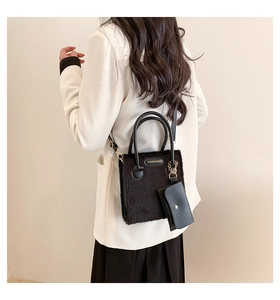 Detail of a black plush crossbody bag on a model wearing a white blazer and black skirt
