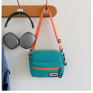 Close-up of blue nylon crossbody bag with orange straps and niu logo detail
