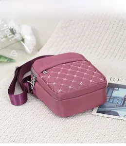 Close-up of quilted burgundy nylon crossbody bag with floral embroidery on white knit