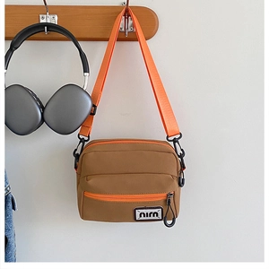 Detail view of khaki canvas crossbody bag with orange strap and headphone accessory