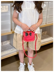 Vue détaillée d'un petit sac rouge avec nœud papillon porté par un enfant en bandoulière