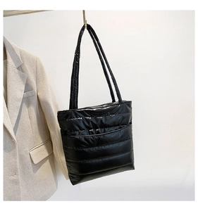 Close-up of black quilted puffer tote bag hanging with stylish business blazer background