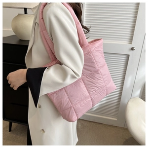 Pink quilted puffer tote bag with padded shoulder strap shown in a casual lifestyle setting