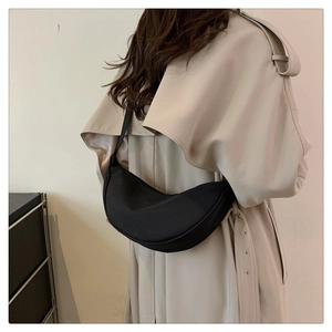Dettaglio della borsa a mezzaluna in nylon nero indossata su un trench beige elegante