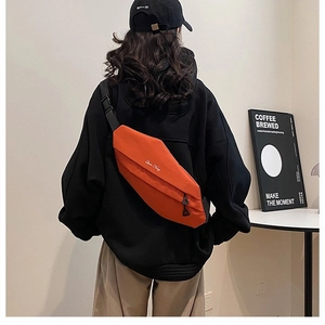 Detail of vibrant orange minimalist chest bag with white embroidery on black hoodie