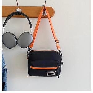 Detail of nylon crossbody bag featuring black body with vibrant orange strap and zipper
