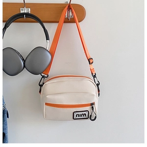 Detail of canvas crossbody bag with orange zipper pocket and adjustable strap hanging on hook