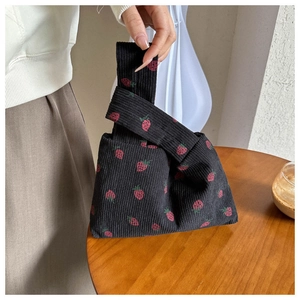 Detail of cute black corduroy wrist bag with red strawberry pattern and single handle loop