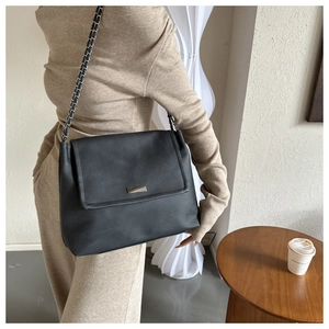 Detail of a black minimalist leather shoulder bag featuring a silver rectangular metal lock