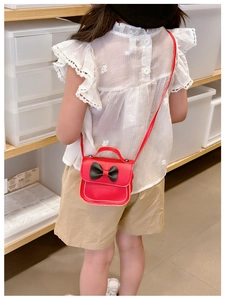 Vue arrière d'une fille portant un mini sac bandoulière en cuir rouge avec un nœud noir