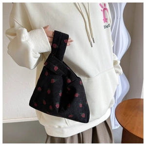 Detail of black corduroy wrist bag with strawberry print held by a model