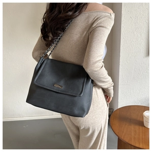 Detail of black leather shoulder bag with metal buckle and chain strap on a model