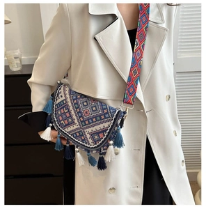 Ethnic crossbody bag with blue tassels and wide woven strap on a white coat