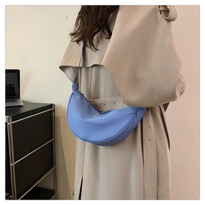 Vista posteriore di una borsa a mezzaluna in nylon azzurro indossata con un trench beige
