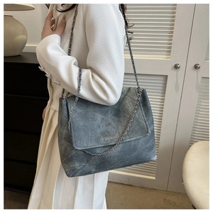 Detail of blue-grey denim textured chain bag with metallic strap on model's shoulder