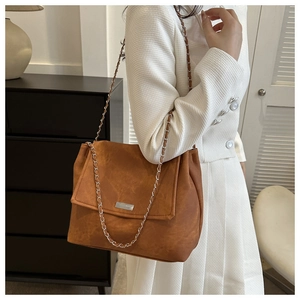 Detail of a brown suede flap bag with metal chain strap and rectangular silver plaque